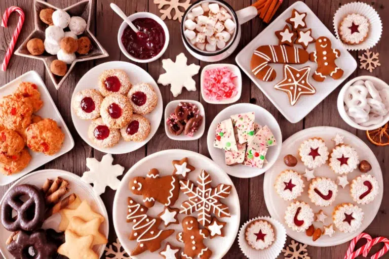 A festive spread of holiday treats showcases traditional Christmas recipes, including panettone, biscotti, and nougat, all beautifully arranged with ornaments and pine branches.