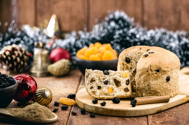 A festive scene featuring a sliced panettone on a wooden board, surrounded by dried fruits, cinnamon sticks, and Christmas decorations, with a focus on Vegan and Vegetarian Christmas Recipes.