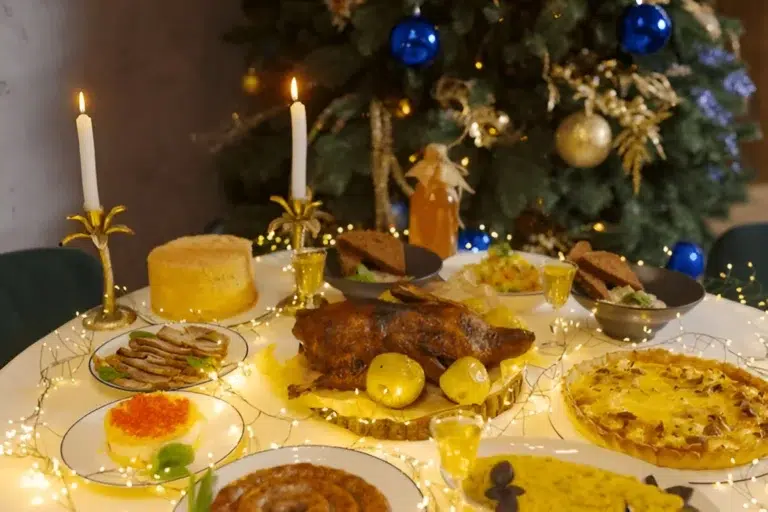 A festive dinner table is set for a Christmas Dinner for a Crowd, featuring a roasted meat centerpiece, surrounded by candles, decorations, and a Christmas tree
