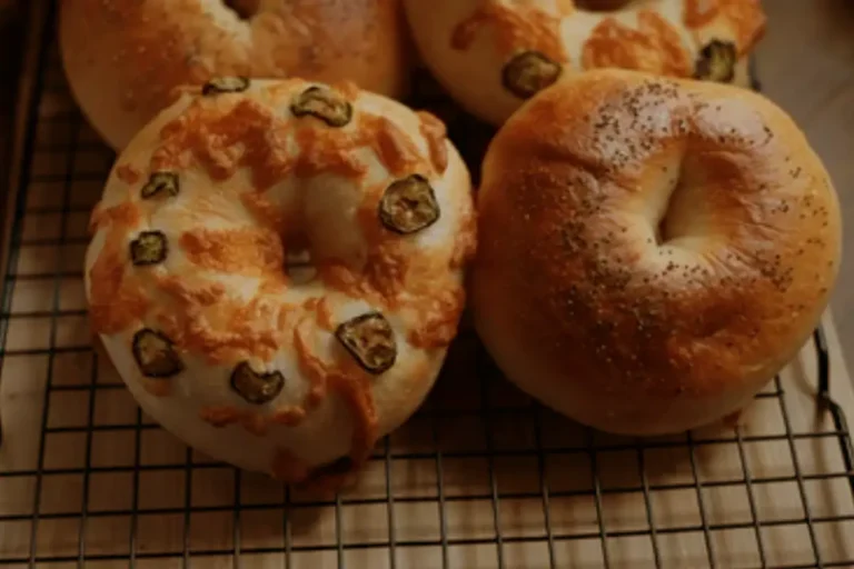 Four sourdough bagels recipe on a cooling rack, two of which are topped with melted cheese and sliced jalapeños, and the other two are plain.